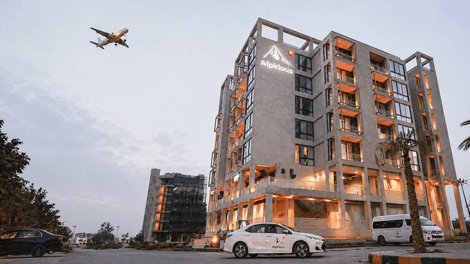 The Alpirious building at dusk with a plane passing overhead